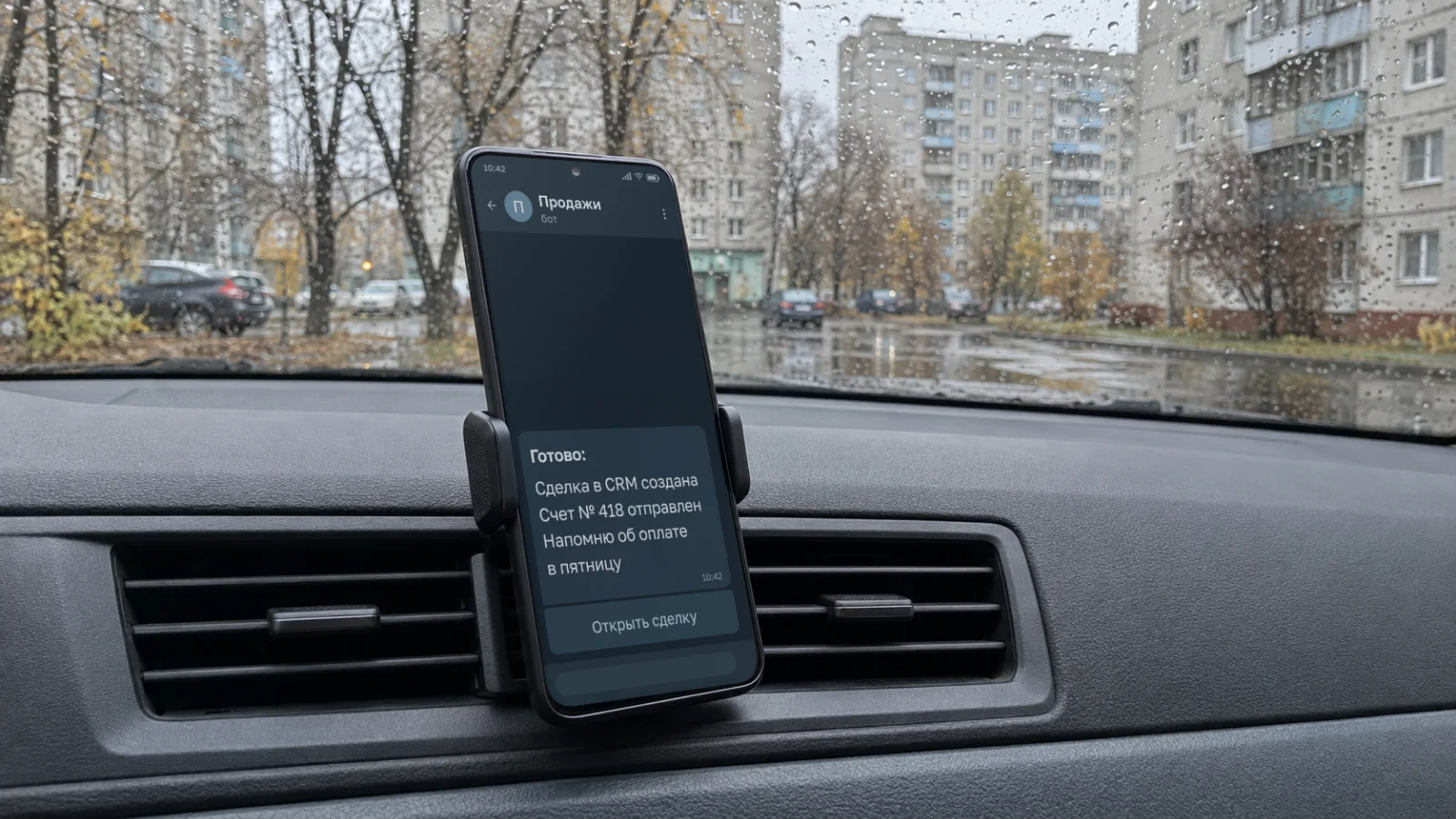 Телефон в держателе в машине, за мокрым от дождя стеклом двор с панельными домами. На экране агент «Продажи» в Telegram сообщает: сделка в CRM создана, счет № 418 отправлен, напомнит об оплате в пятницу. Руководитель в дороге, а работу уже сделал агент